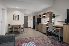 A modern kitchen with a microwave, refrigerator, and dining area with chairs and a table. - Home2 Suites By Hilton Hickory (Hickory)