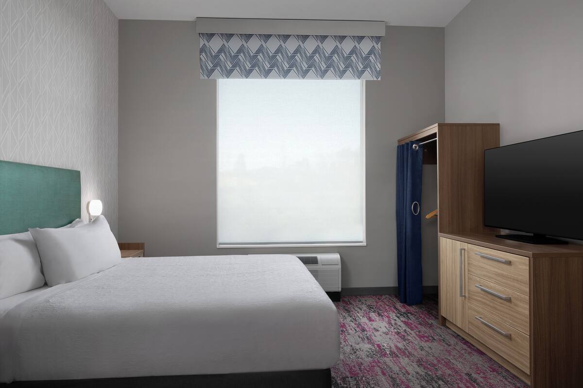 A hotel room with a bed, a television, a wardrobe, and a window with a view.