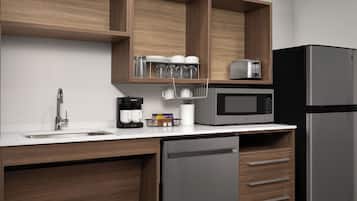 Une cuisine moderne dotée d’un réfrigérateur en acier inoxydable, d’un four à micro-ondes encastré, d’une machine à café et de meubles de rangement en bois.