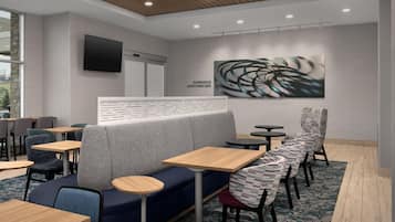 A modern cafe interior with seating arrangements, a flat-screen TV, and a wall-mounted artwork.