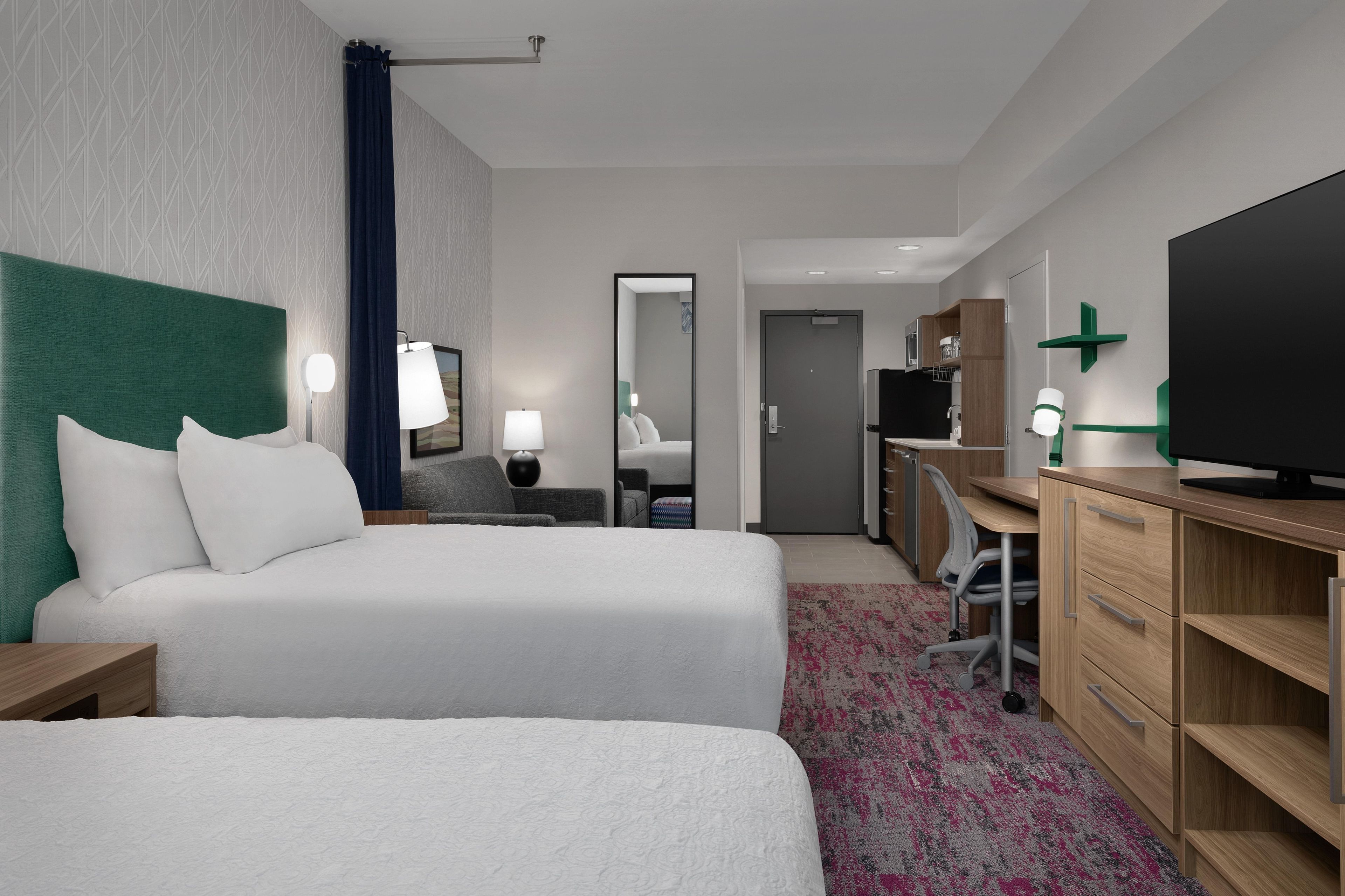A hotel room with two beds, a desk, a television, and a bathroom visible in the background.