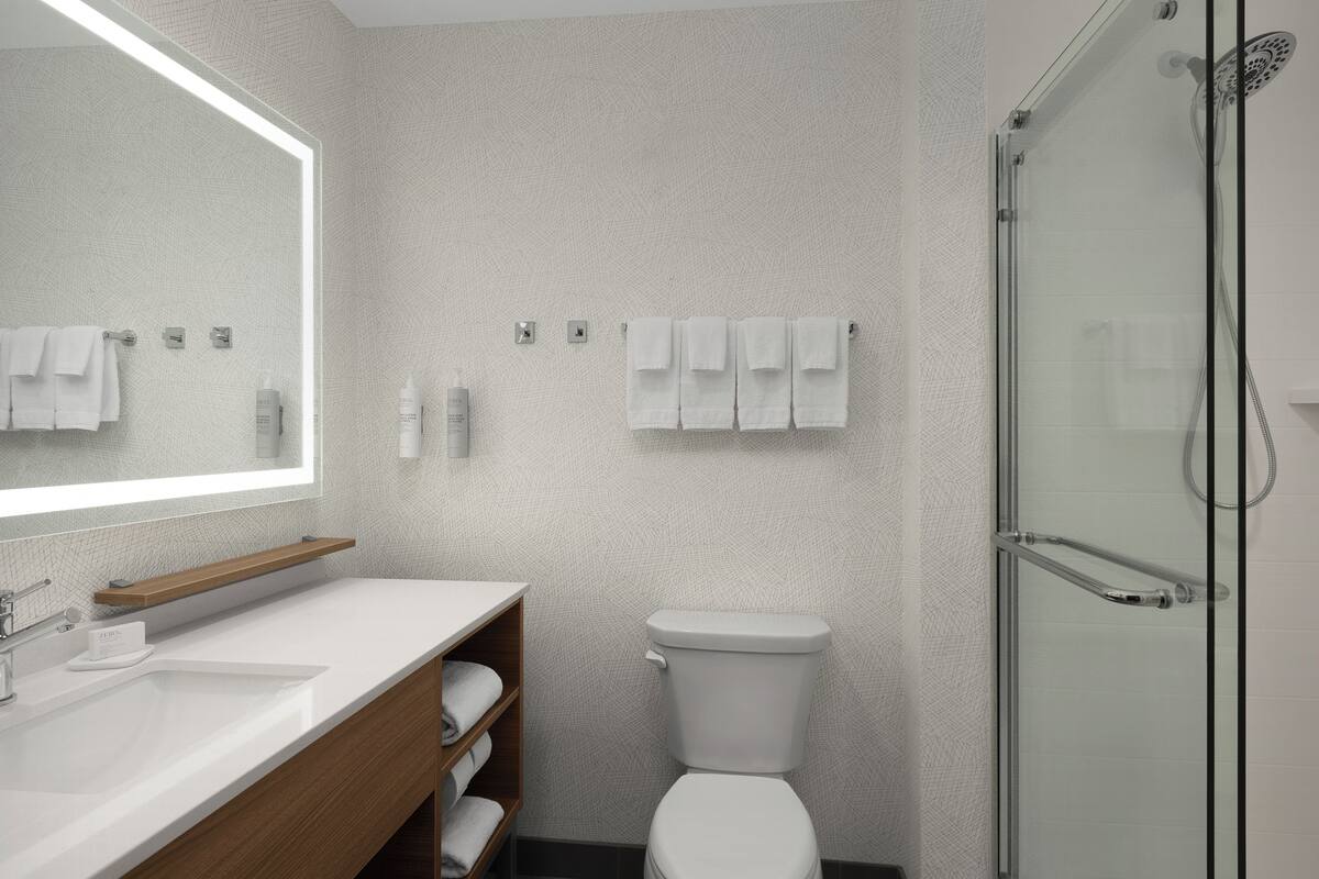 A modern bathroom with a large mirror, white sink, wooden vanity, toilet, and glass shower enclosure.