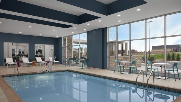 A swimming pool with lounge chairs and tables, large windows, and a view of the outside. - Home2 Suites By Hilton Hickory (Hickory)