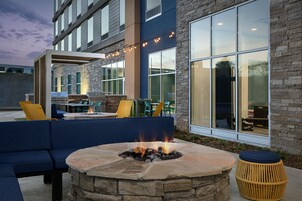 An outdoor seating area with a stone fire pit, blue furniture, and a building with large windows and stone facade.