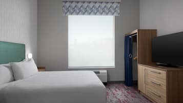 Quarto de hotel com uma cama, televisão, guarda-roupa e janela com cortina estampada.