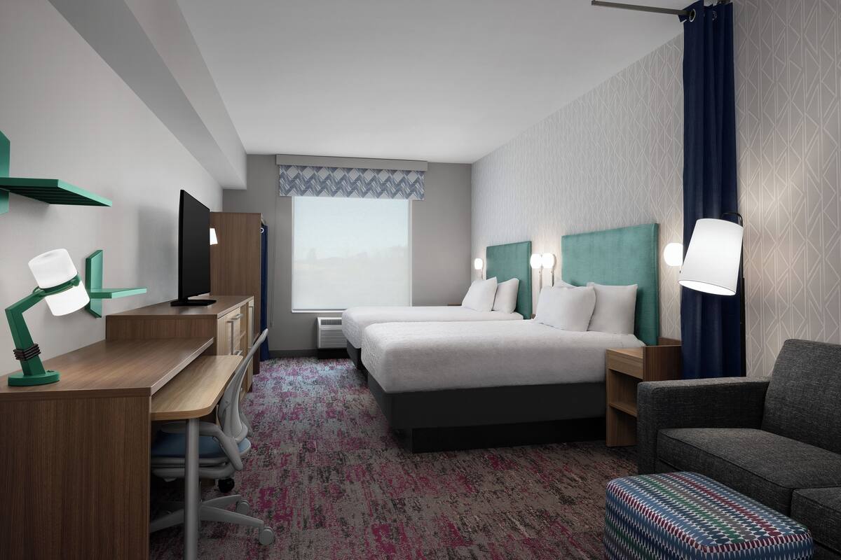 A hotel room with a bed, desk, chair, TV, and a window with curtains.