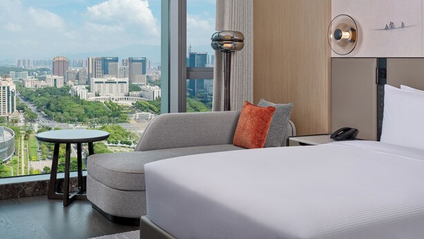 A hotel room with a large bed, a sofa, a small table, and a view of a cityscape. - Hilton Huizhou (Huizhou)