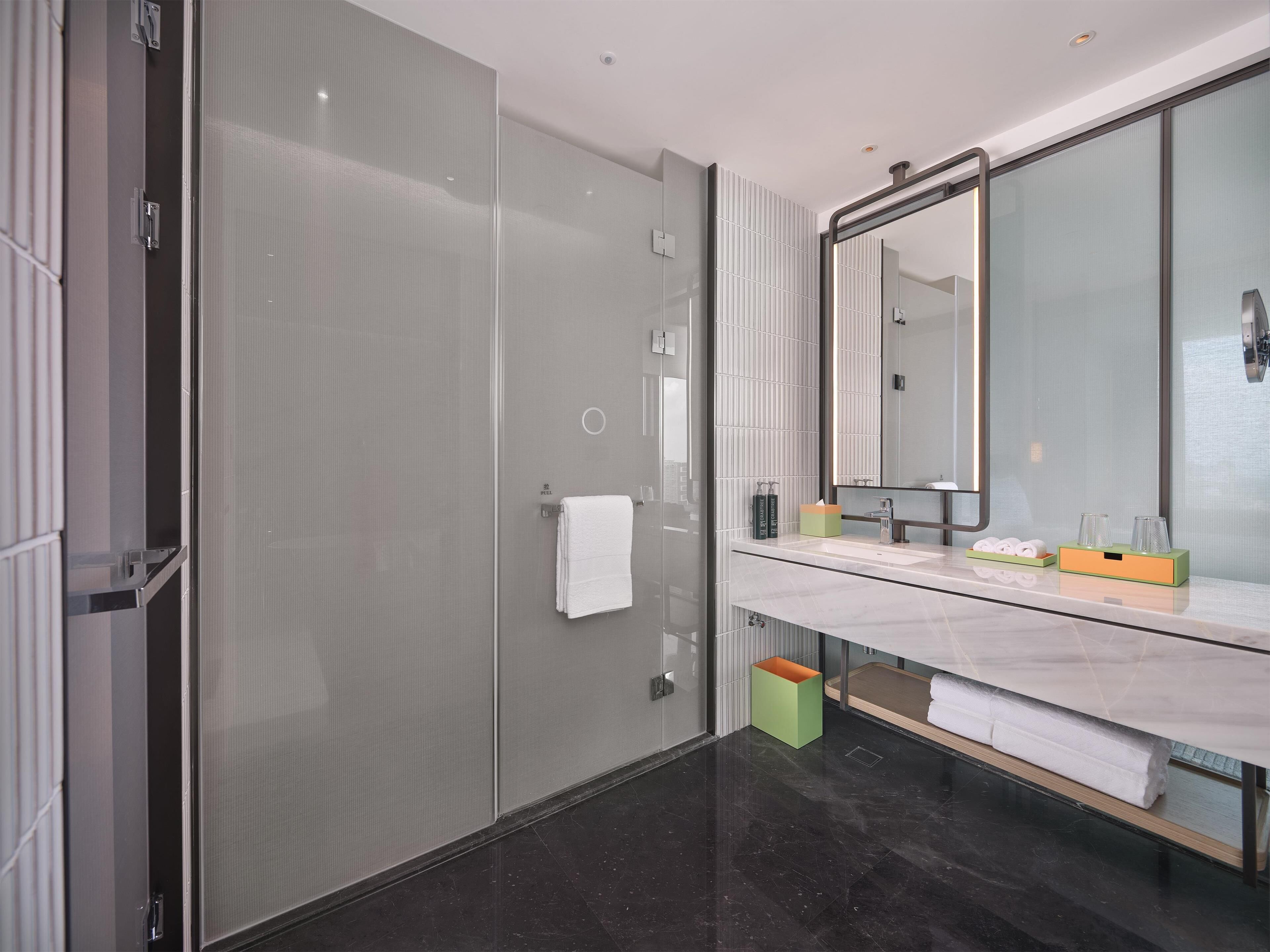 Un baño moderno con cabina de ducha de vidrio, un espejo grande y un tocador de mármol con artículos de aseo.