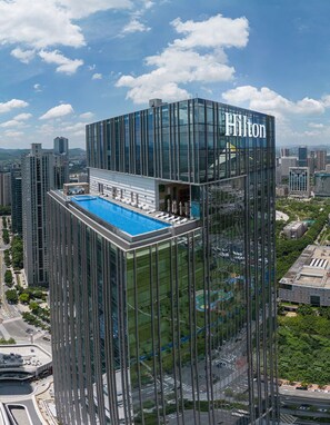 A high-rise building with a glass facade, a rooftop pool, and the Hilton logo.