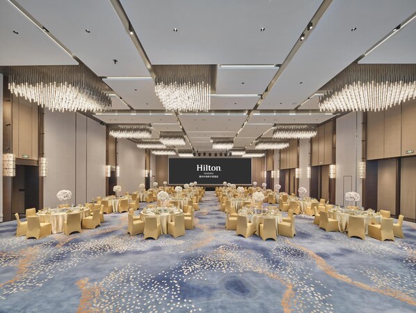 A spacious conference room with round tables, beige chairs, and a large screen displaying "Hilton." - Hilton Huizhou (Huizhou)