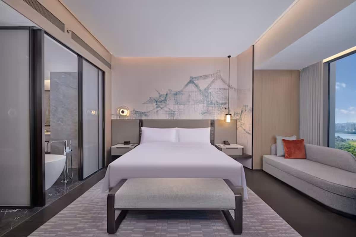 Ein modernes Hotelzimmer mit einem großen Bett, einer Couch, einer Bank, einem Badezimmer mit Badewanne und Blick auf die Stadt.