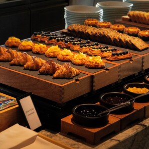 Ein Buffet mit verschiedenen Backwaren und Desserts, darunter Croissants und Obsttorten.