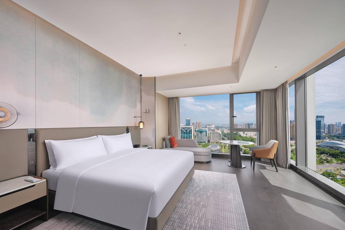 Ein modernes Hotelzimmer mit einem großen Bett, einer kleinen Sitzecke und einem Balkon mit Blick auf die Stadt.
