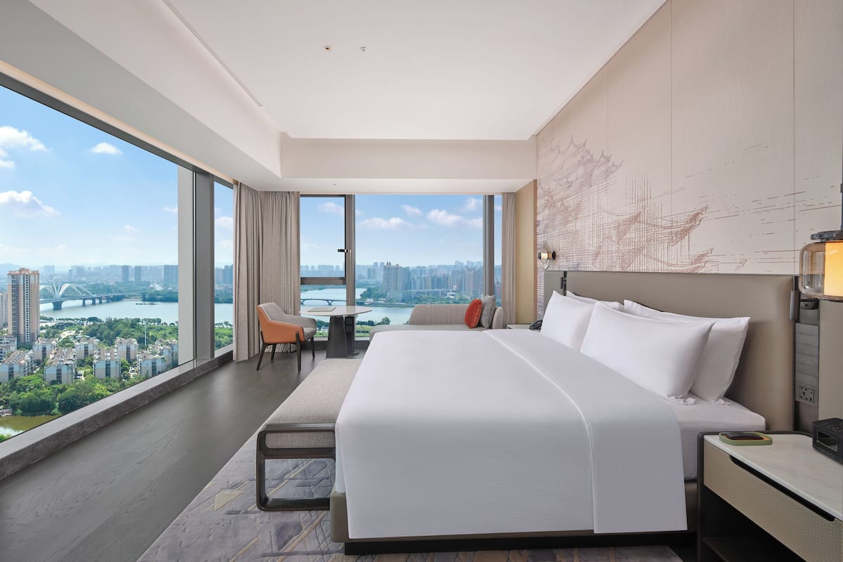 Ein modernes Hotelzimmer mit einem großen Bett, einem Schreibtisch und Blick auf eine Skyline durch große Fenster.