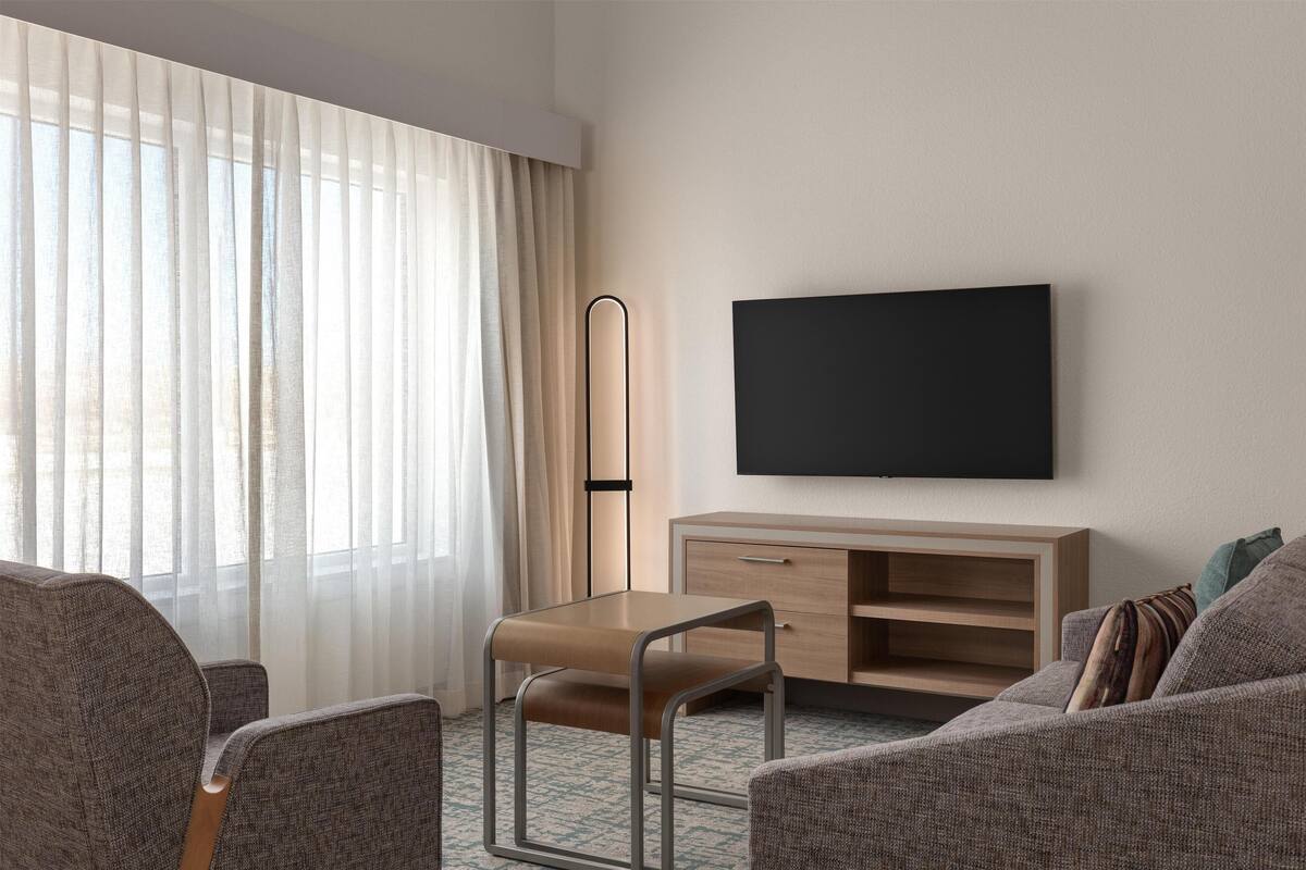 Ein Hotelzimmer mit Bett, Wandfernseher, Schreibtisch mit Schubladen und Stuhl.