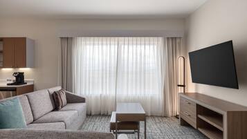 Quarto de hotel moderno com sofá, mesa pequena, televisão e máquina de café.