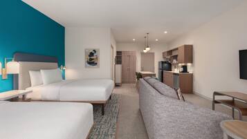 Una habitación de hotel moderna con dos camas, un sofá, un comedor y una kitchenette.