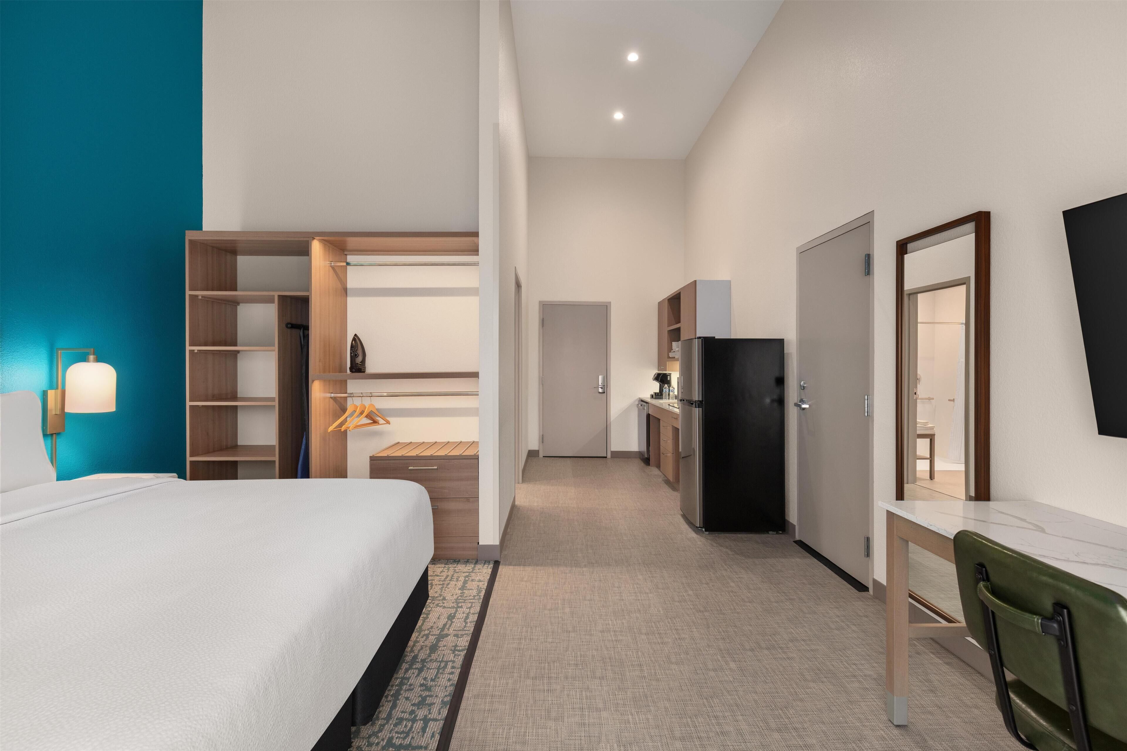 Een hotelkamer met een bed, bureau, kledingkast, spiegel en een kitchenette.