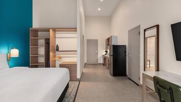 Een hotelkamer met een bed, bureau, kledingkast, spiegel en een kitchenette.