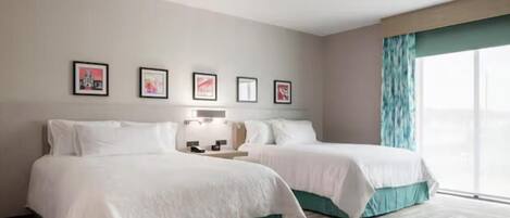 A hotel room with two beds, a nightstand, a lamp, and a window with curtains.