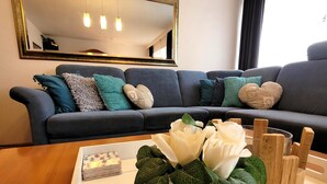 A living room with a dark blue sofa, multiple pillows, a white vase with white flowers, and a wooden coffee table. - Apartment in Winterberg Near Kappe Mountain (Winterberg)