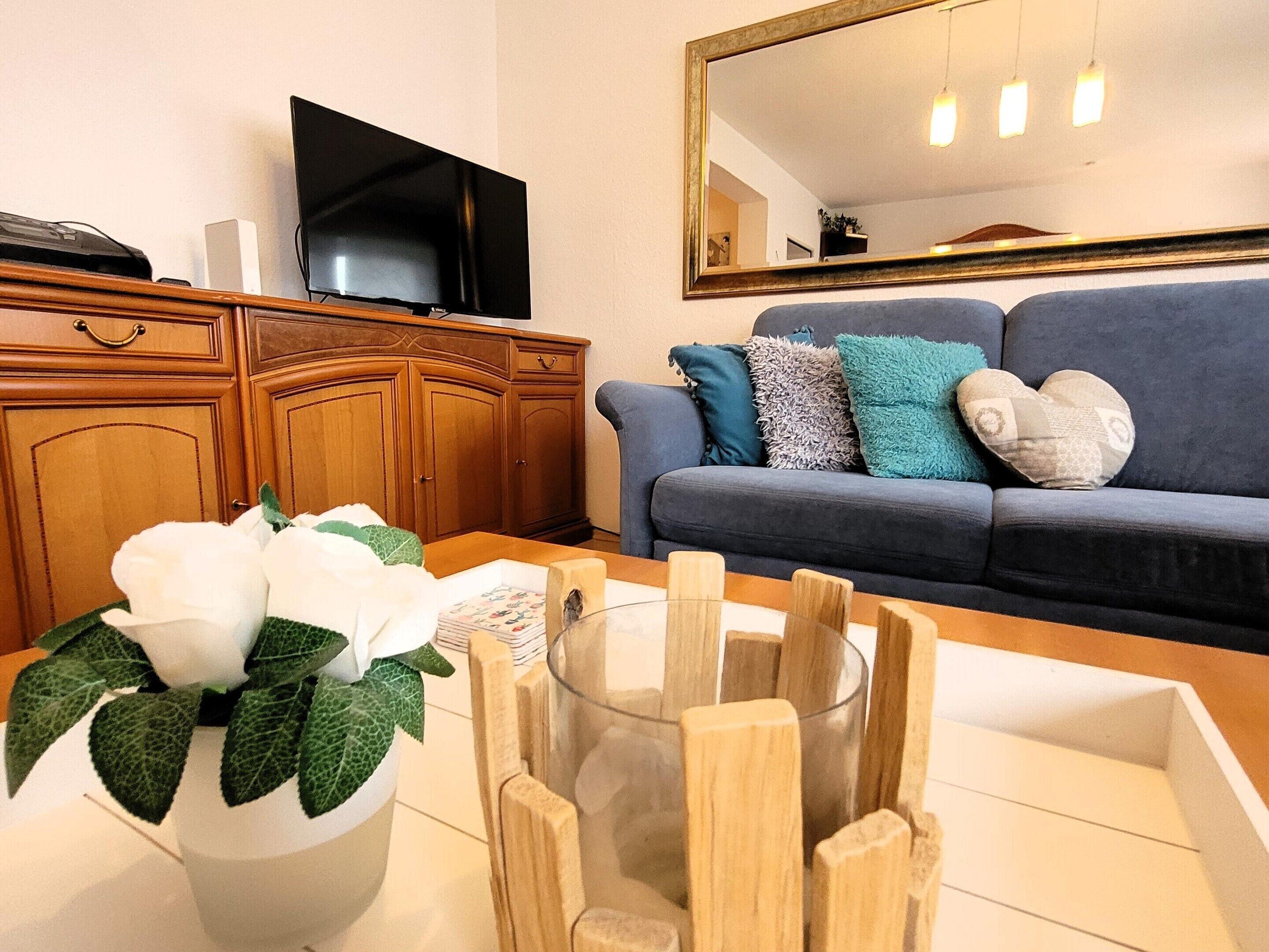 A living room with a sofa, a television, wooden cabinets, and a vase with white flowers.