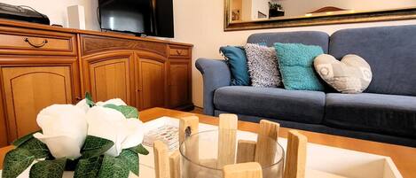 A living room with a sofa, a television, wooden cabinets, and a vase with white flowers.