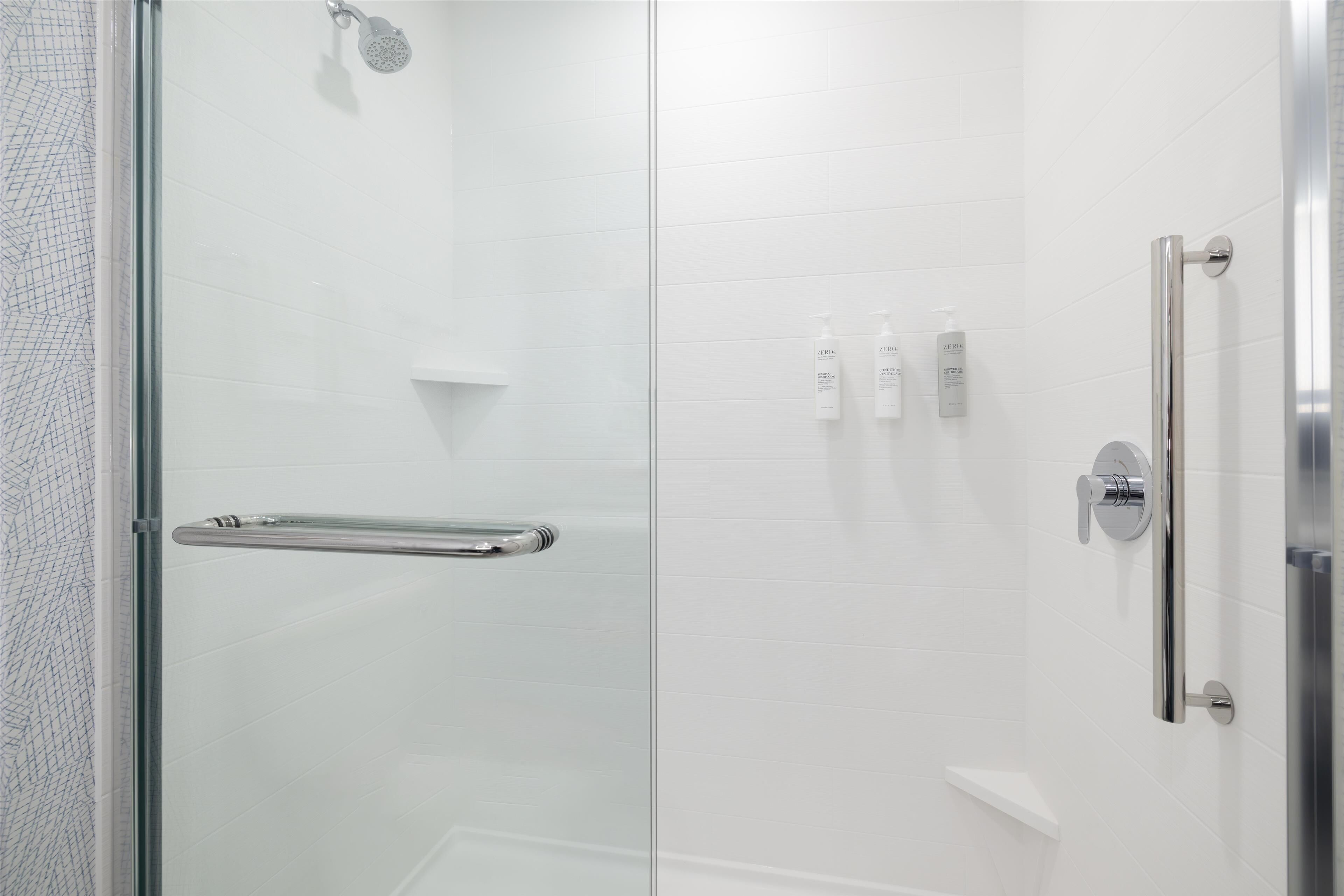 Un área de ducha moderna con puerta de cristal, barra de apoyo y ducha.