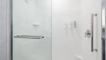 Un área de ducha moderna con puerta de cristal, barra de apoyo y ducha.