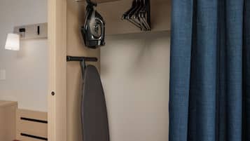 Une petite pièce comprenant une armoire en bois, un fer à repasser et un ensemble de cintres.