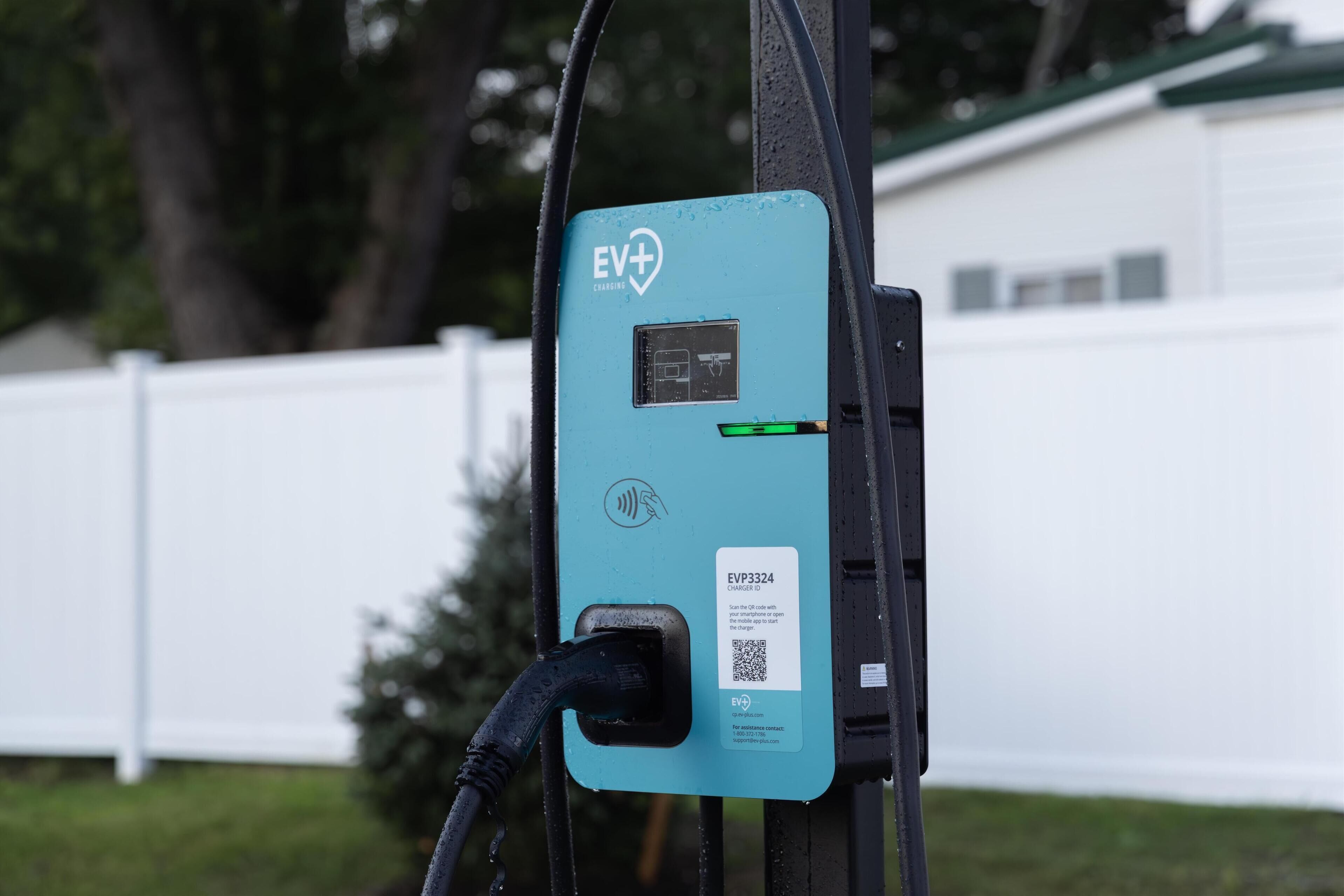 An EV charging station with a digital display, a QR code for the charger ID, and a charging cable connected.
