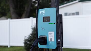 An EV charging station with a digital display, a QR code for the charger ID, and a charging cable connected.