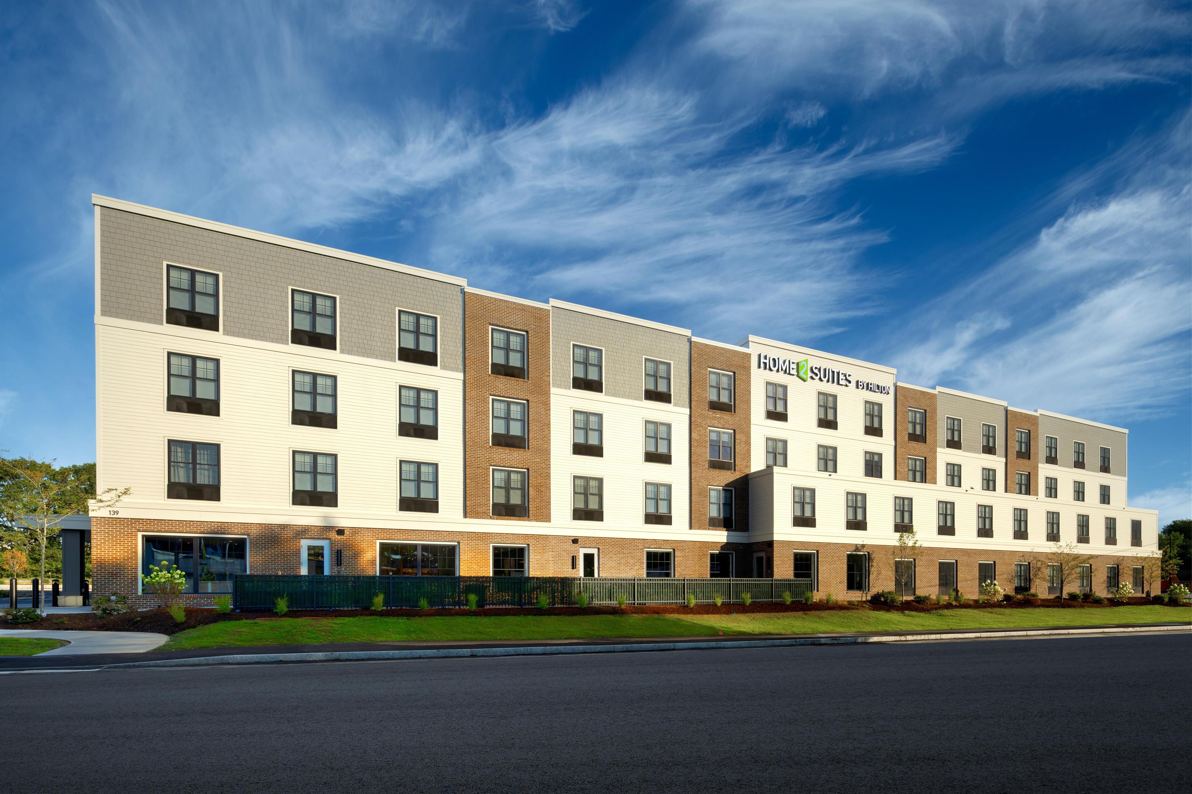 Et moderne hotel i flere etager med murstens- og hvide facadevægge, store vinduer og et skilt, der angiver, at det er et hotel med lejligheder.