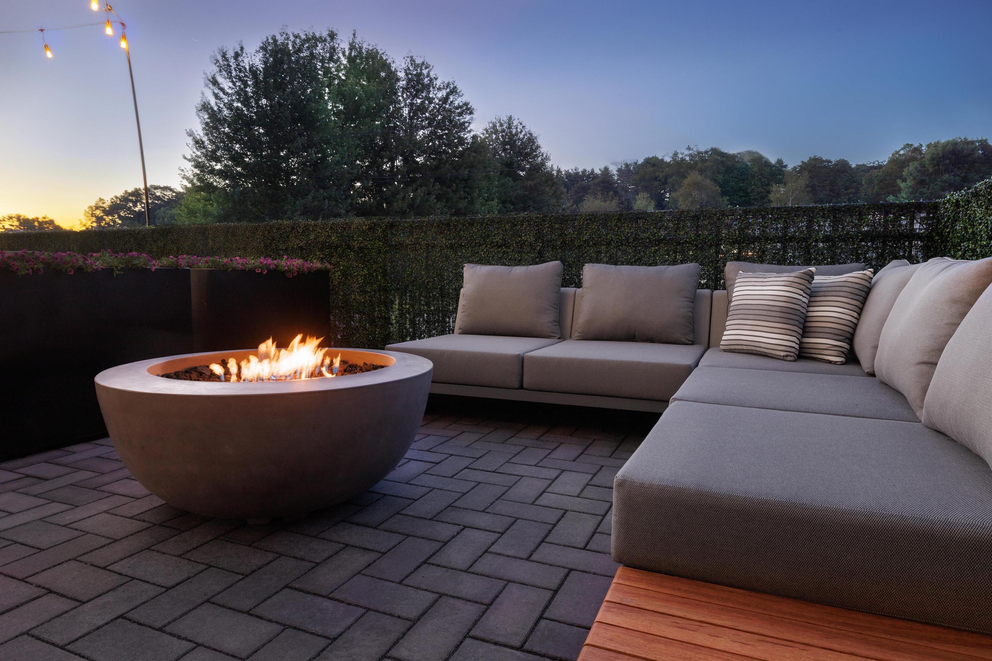 An outdoor seating area with a fire pit, a sofa, and a hedge.
