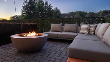 An outdoor seating area with a fire pit, a sofa, and a hedge.
