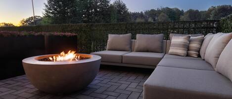An outdoor seating area with a fire pit, a sofa, and a hedge.
