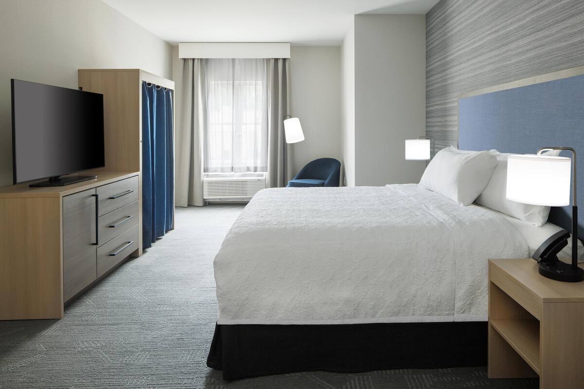 A hotel room with a bed, a television, a desk, a chair, and a window with curtains.