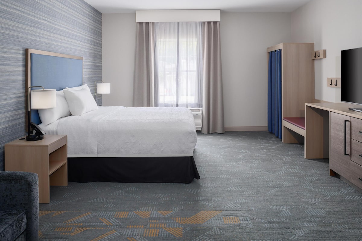 A hotel room with a bed, bedside tables, a TV, a wardrobe, and a window with curtains.