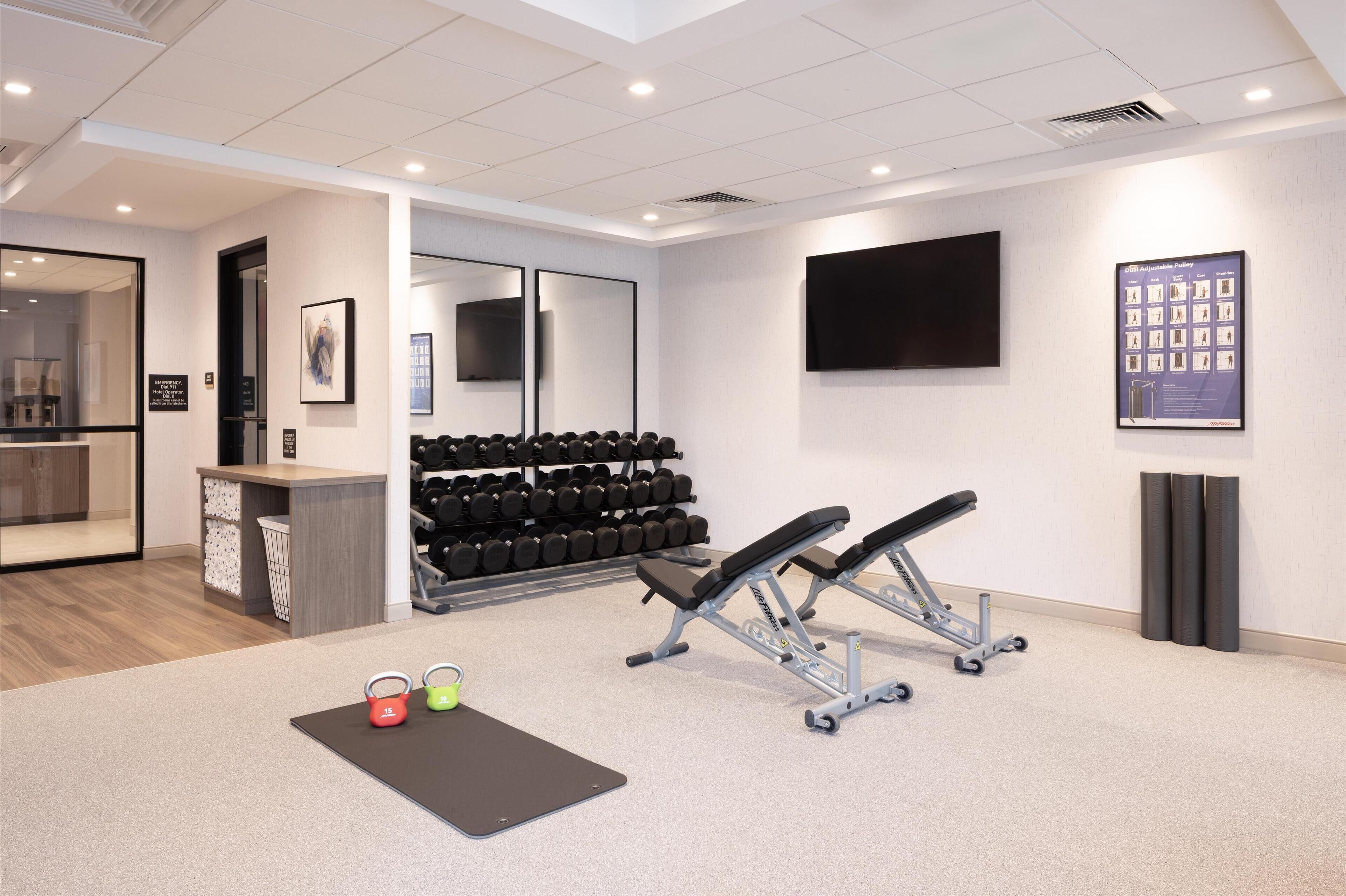 A modern gym with exercise equipment, a wall-mounted TV, and a shoe rack.