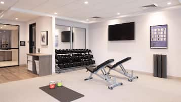 A modern gym with exercise equipment, a wall-mounted TV, and a shoe rack.