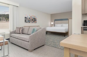 Habitación de hotel con sofá, cama, mesa y vistas a la montaña.