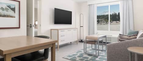 Ett modernt hotellrum med en matplats, en soffa, en TV och utsikt över ett berg och vatten.
