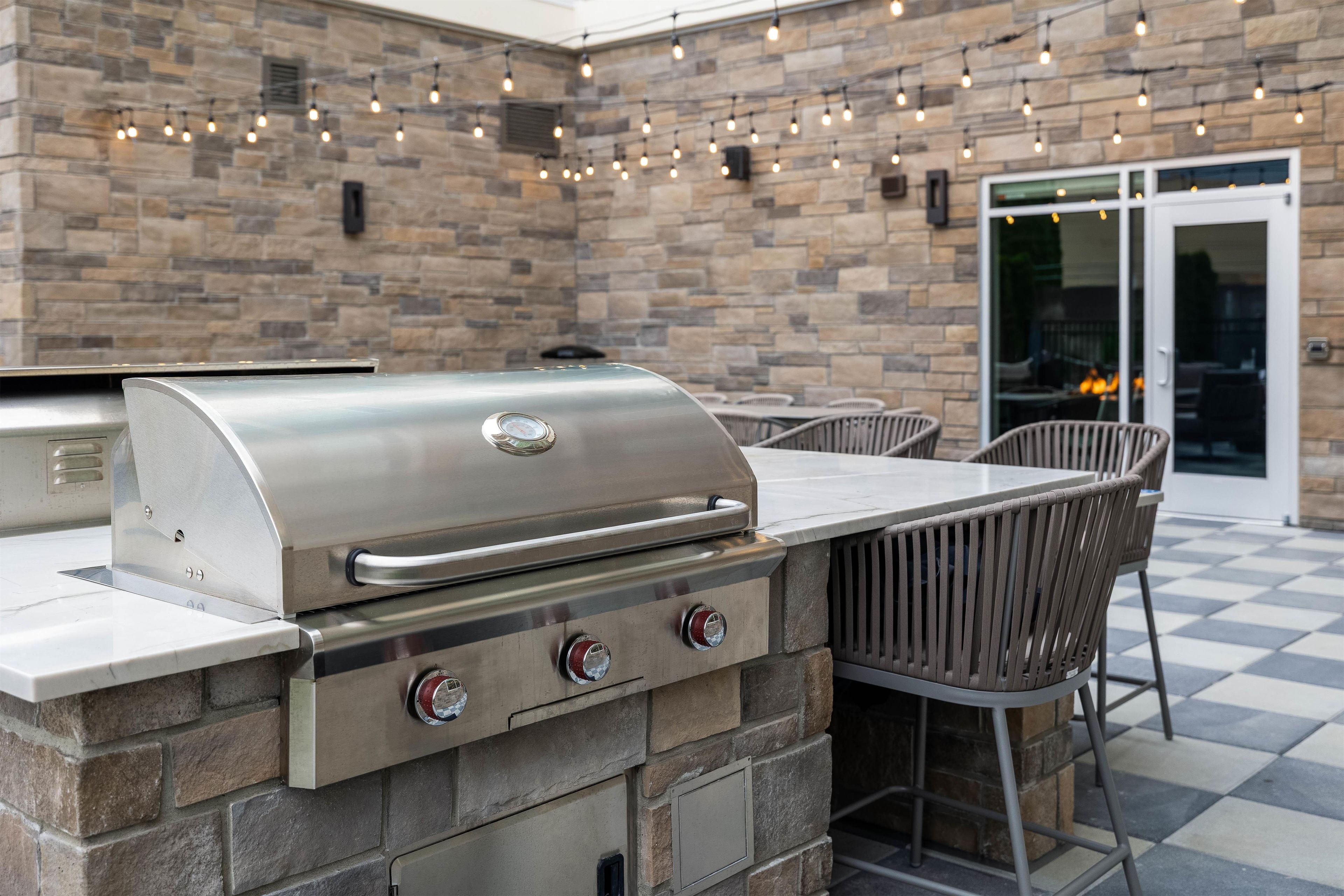 An outdoor kitchen with a built-in grill, stone wall, and string lights.