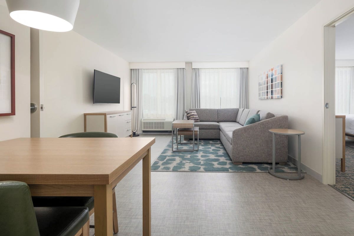 A modern, well-lit living room with a sofa, a small table, and a TV mounted on the wall.