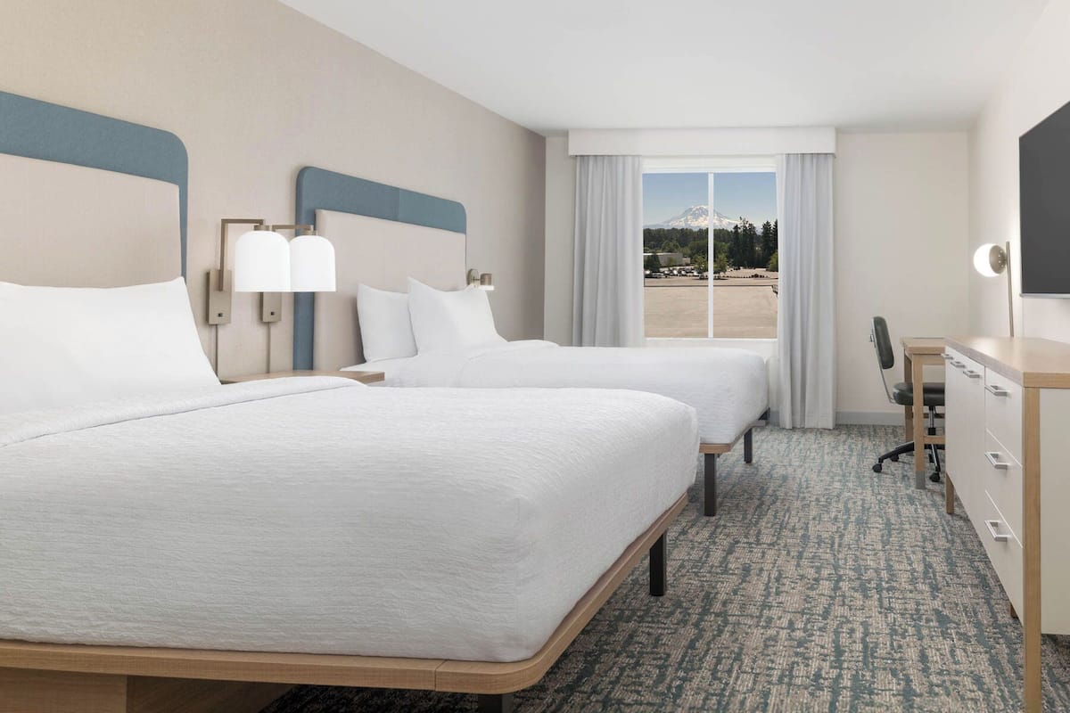 A hotel room with two beds, a desk, and a view of a mountain and beach.