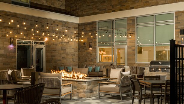 An outdoor patio area with stone walls, a fire pit, string lights, and seating arrangements.