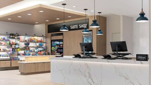 A hotel suite shop with a marble counter, wooden ceiling, and various snacks and beverages on shelves.