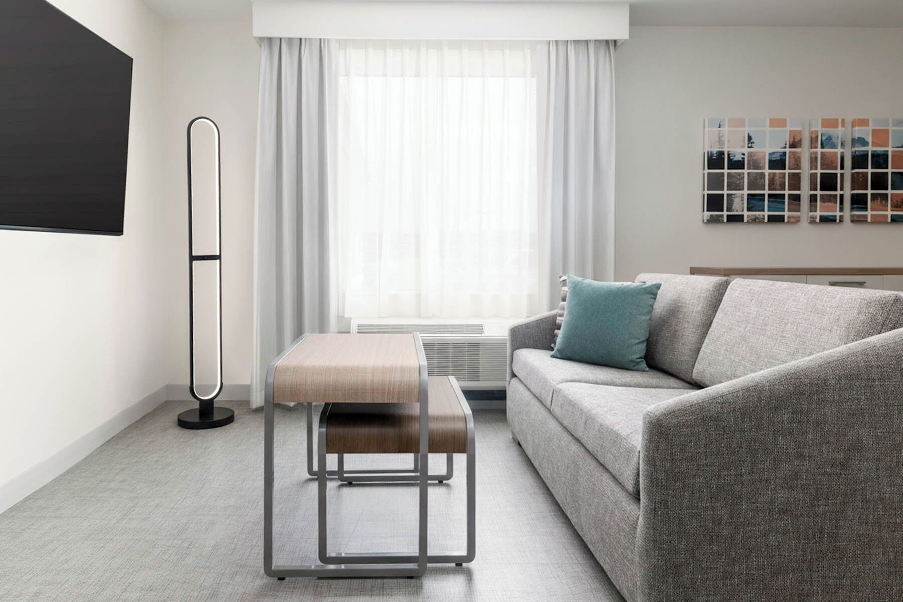 A modern living room with a grey sofa, a wooden bench, a floor lamp, and a large window with sheer curtains.