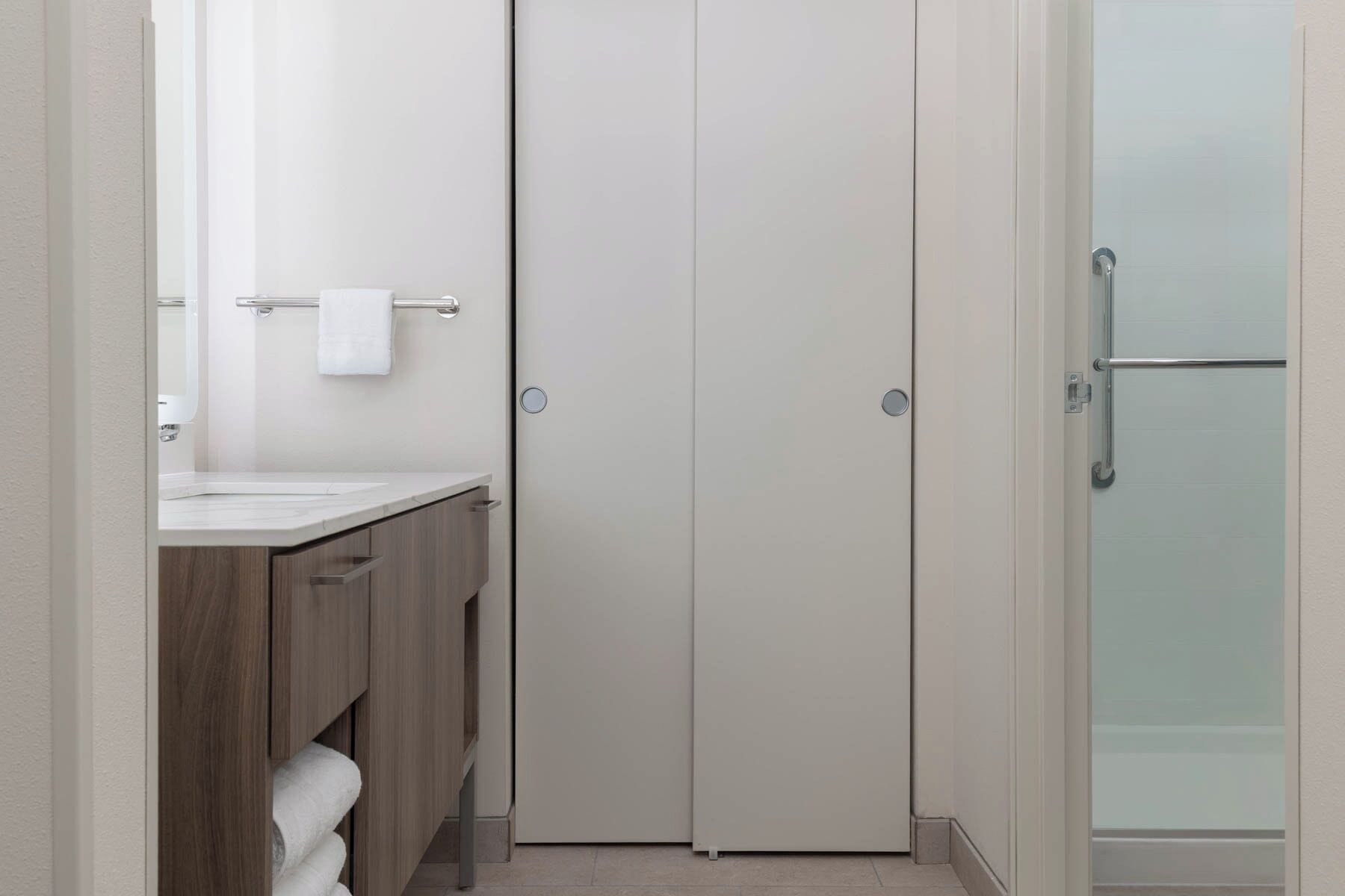 A modern bathroom with a wooden vanity, a white sink, and a glass shower enclosure.