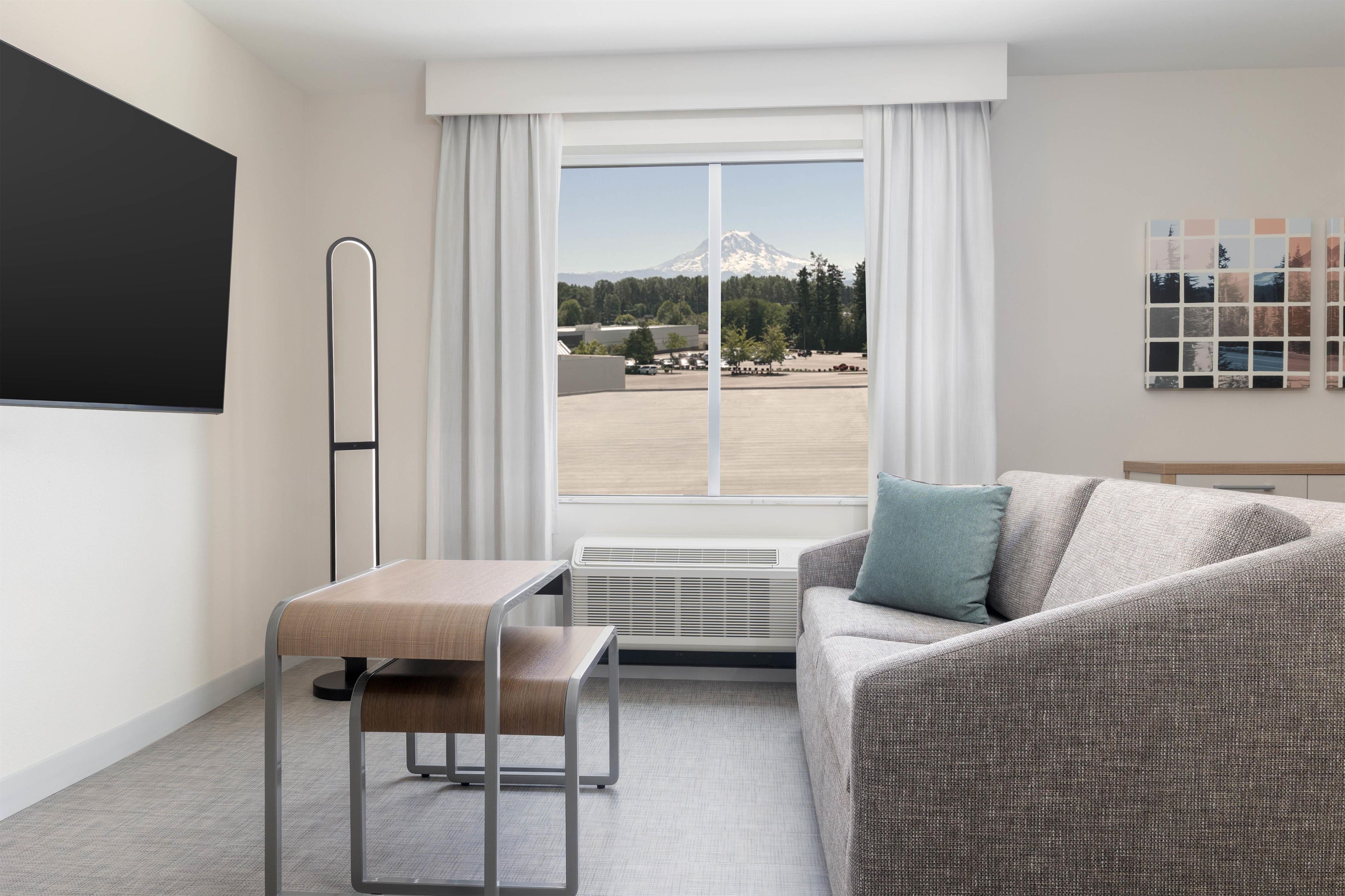 A hotel room with a bed, a desk, a chair, a radiator, and a large window with a view of a mountain.